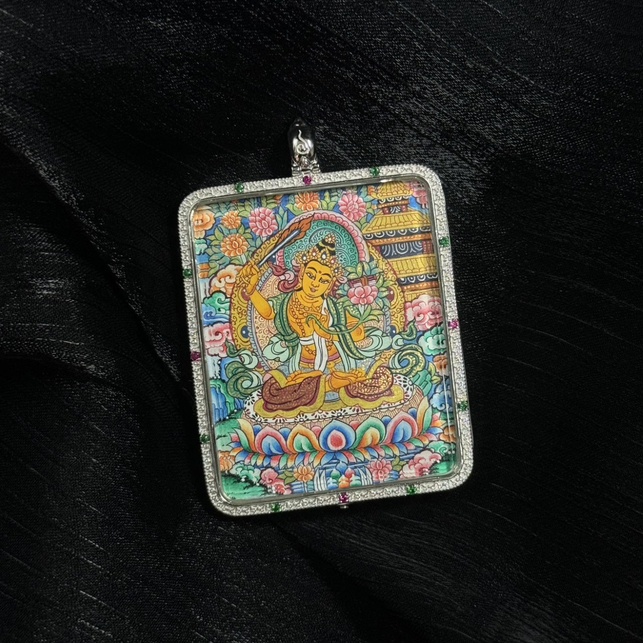 Close view of a Manjushri Bodhisattva mini thangka pendant showing detailed mineral pigment painting, lotus base, and traditional Tibetan iconography inside a silver pendant case.