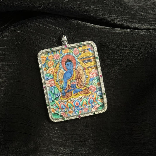 Close-up view of a hand-painted Medicine Buddha mini thangka pendant featuring vibrant mineral pigments, traditional lotus throne, halo, and ornate floral background details.