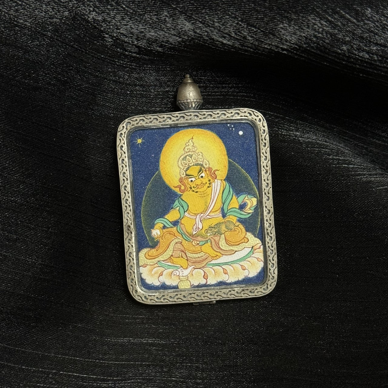 Close-up of Yellow Jambhala mini thangka pendant showing hand-painted deity details, mineral pigment layering, and traditional silver casing structure