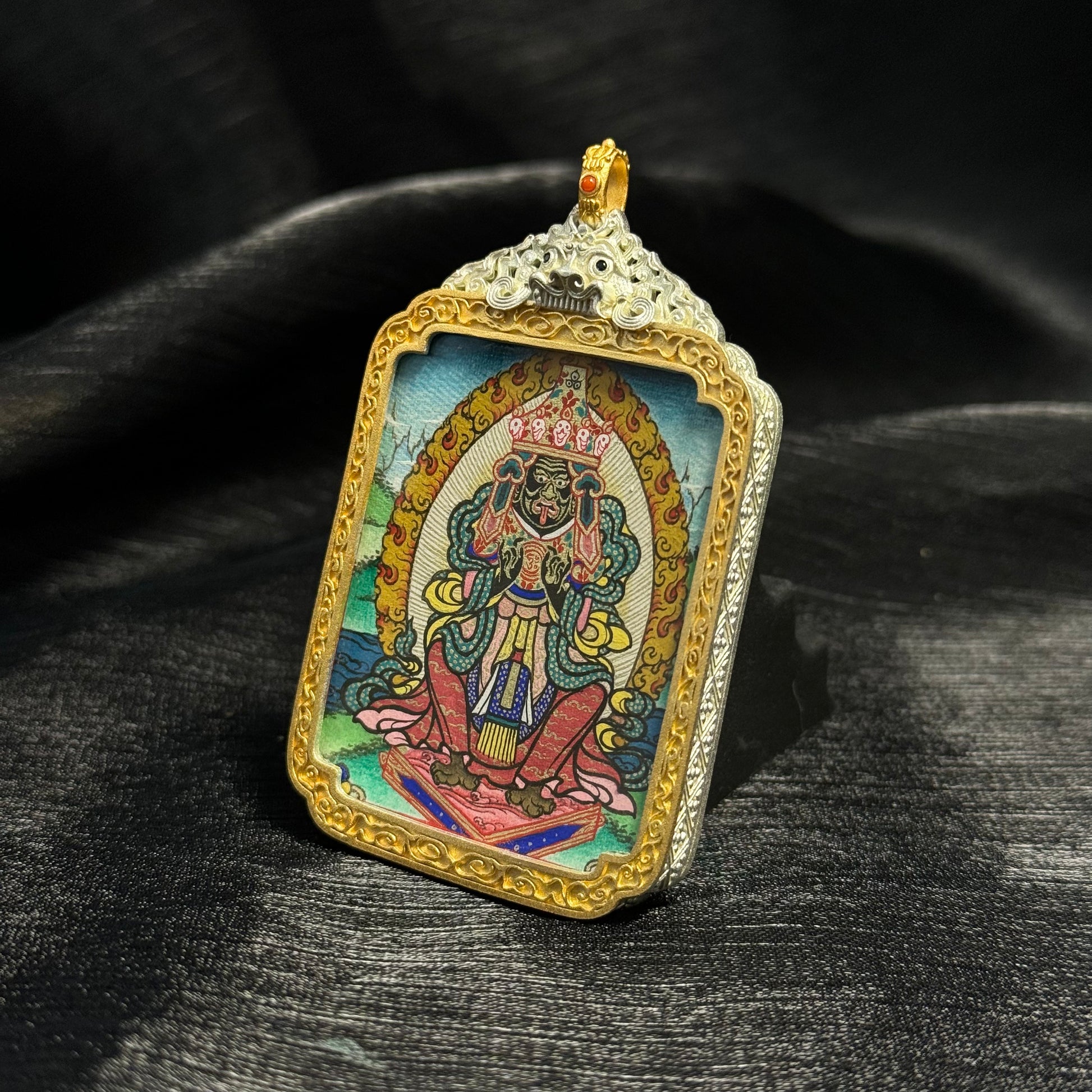 Angled view of Zaki Lhamo hand-painted miniature thangka pendant highlighting mineral pigment colors, detailed linework, and decorative gold frame.