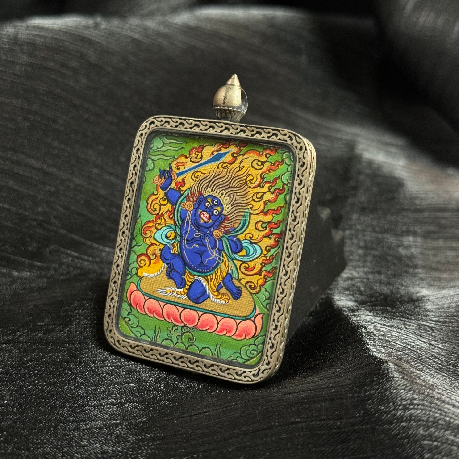 Close angled view of Acalanatha Wisdom King mini thangka pendant with vibrant mineral pigments and traditional Rebgong thangka painting style.