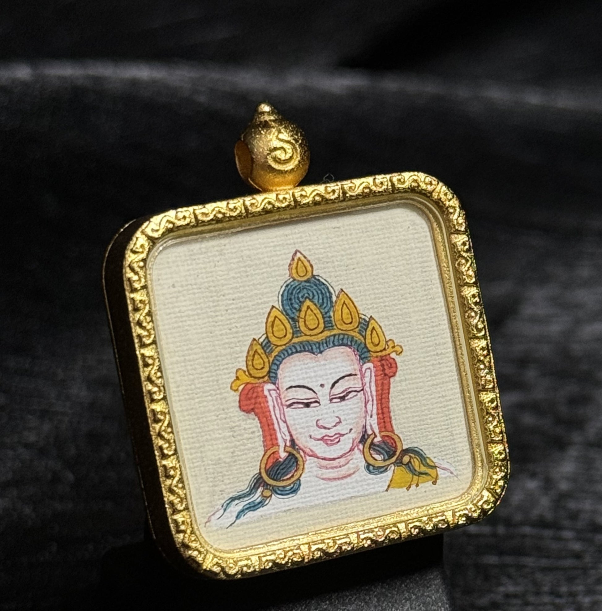 Close perspective of Chenrezig (Four-Armed Avalokiteshvara) miniature thangka painting, highlighting the delicate facial lines, crown ornament details, mineral pigment colors, and the embossed gold pendant frame crafted in traditional Tibetan style.