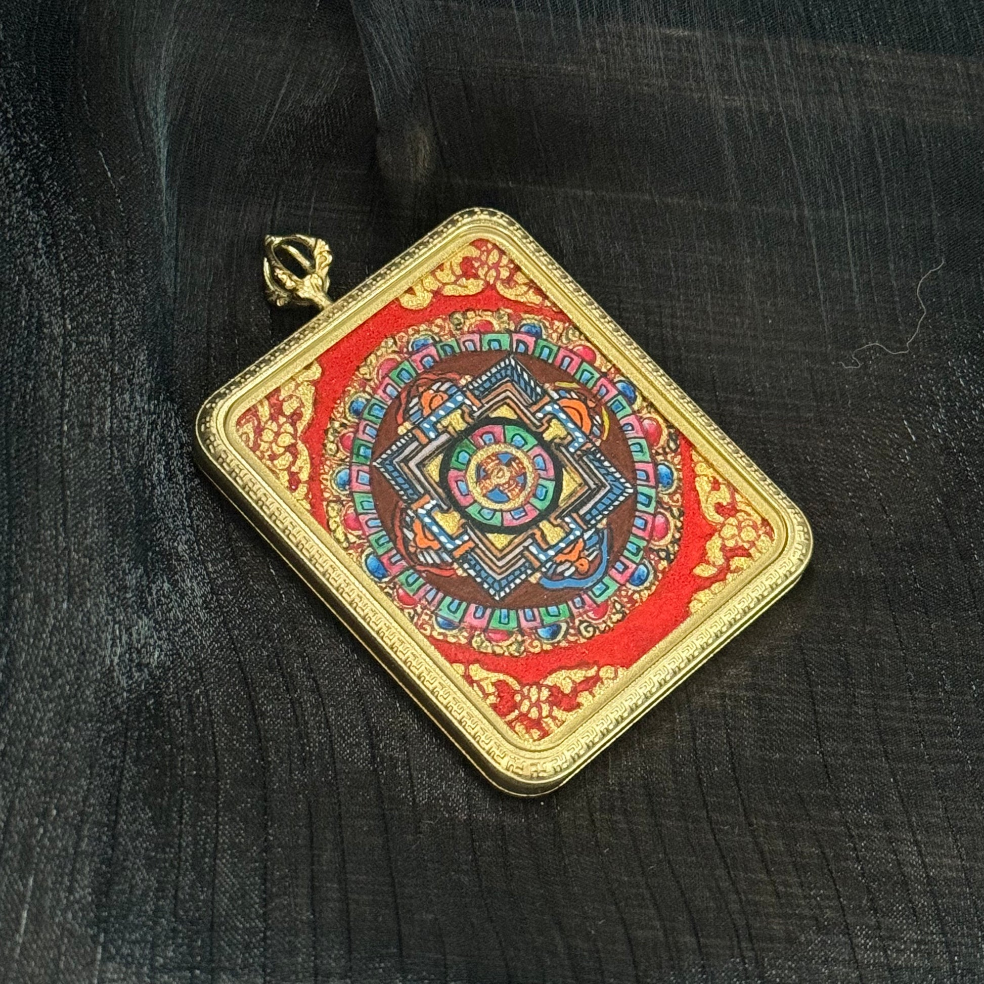 Square Nepal mandala thangka pendant displayed at an angle, showing intricate geometric mandala layers painted with mineral pigments and surrounded by a decorative gold-tone pendant frame.
