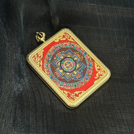 Square Nepal mandala thangka pendant displayed at an angle, showing intricate geometric mandala layers painted with mineral pigments and surrounded by a decorative gold-tone pendant frame.