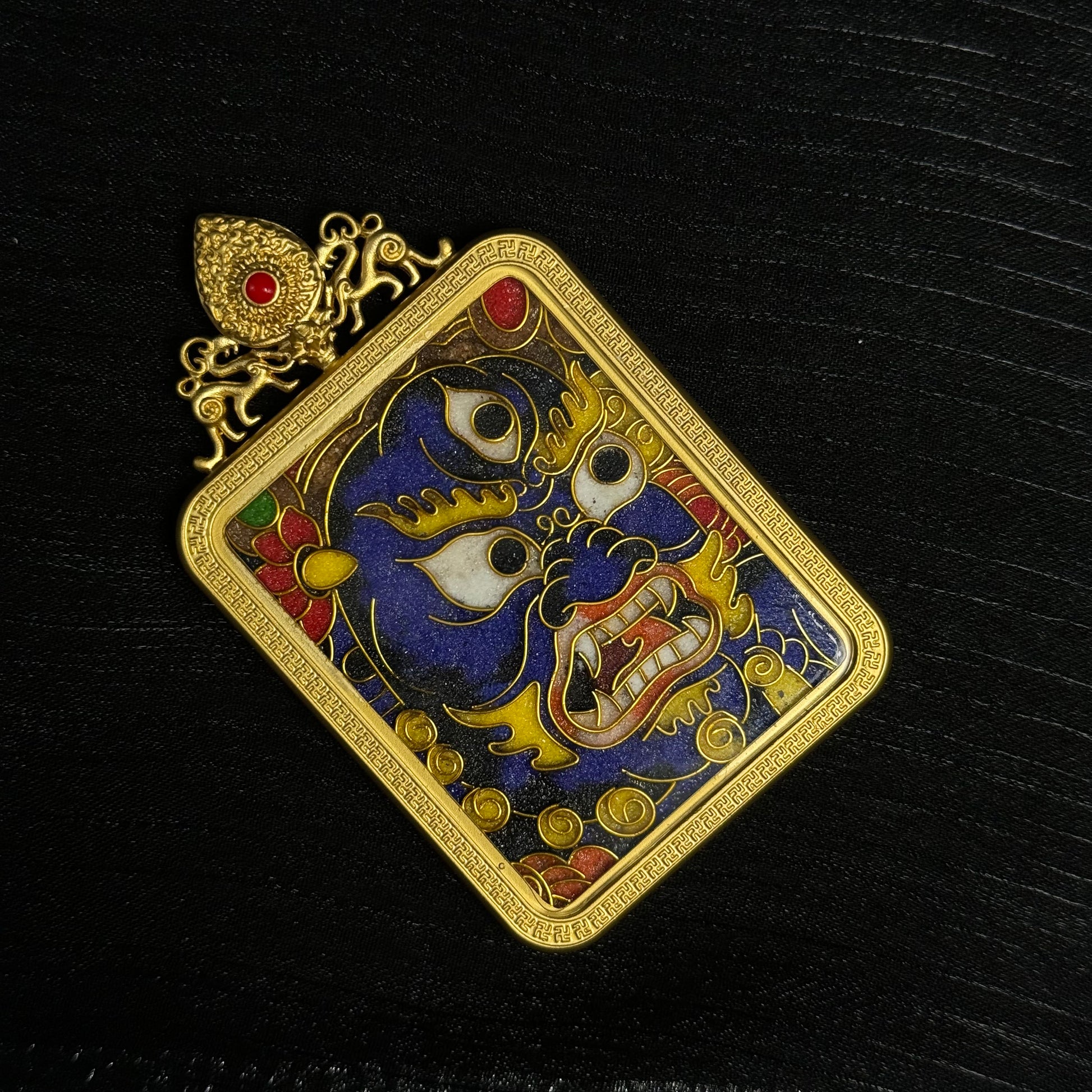 Detailed view of handcrafted Black Jambhala cloisonné enamel mini thangka pendant showing fierce deity face motif, layered enamel colors, and ornate gold-plated frame
