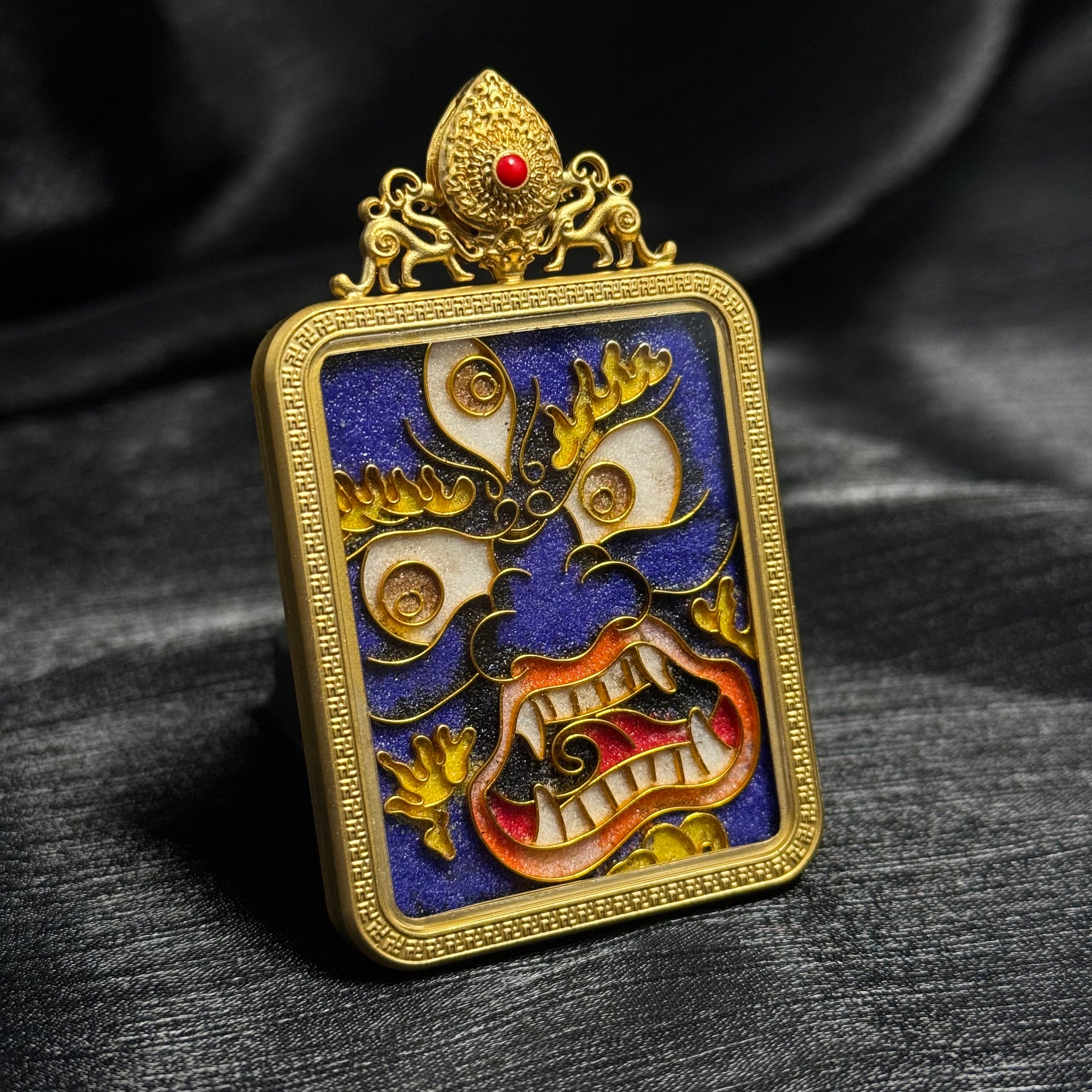 Detailed view of Six-Armed Mahakala pendant featuring traditional Tibetan protector face motif with vivid blue enamel background and gold-plated decorative frame