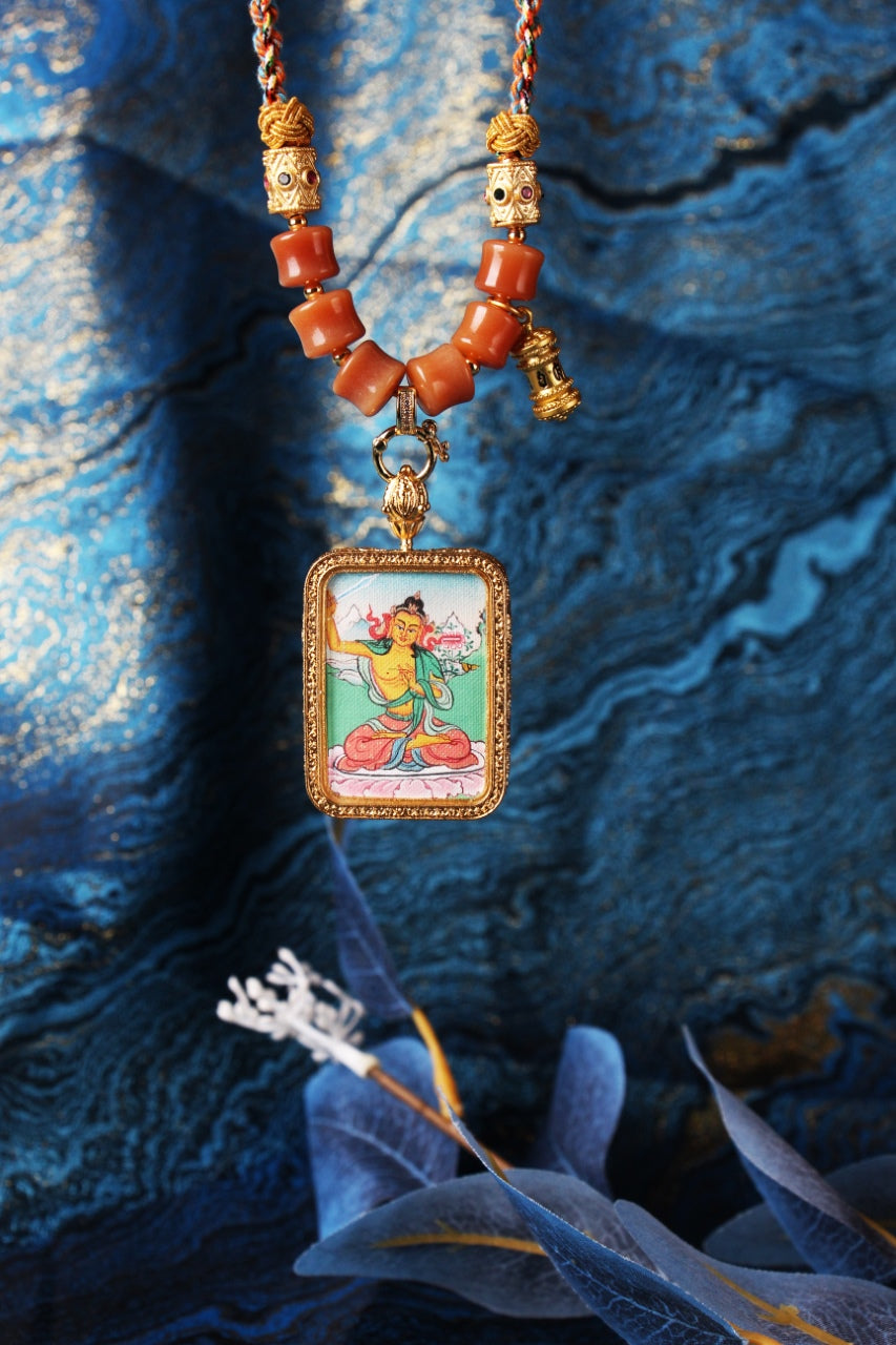 Hanging display of Manjushri mini thangka pendant with a rectangular metal bezel, braided cords, beadwork sections, and the double-sided protective pendant structure