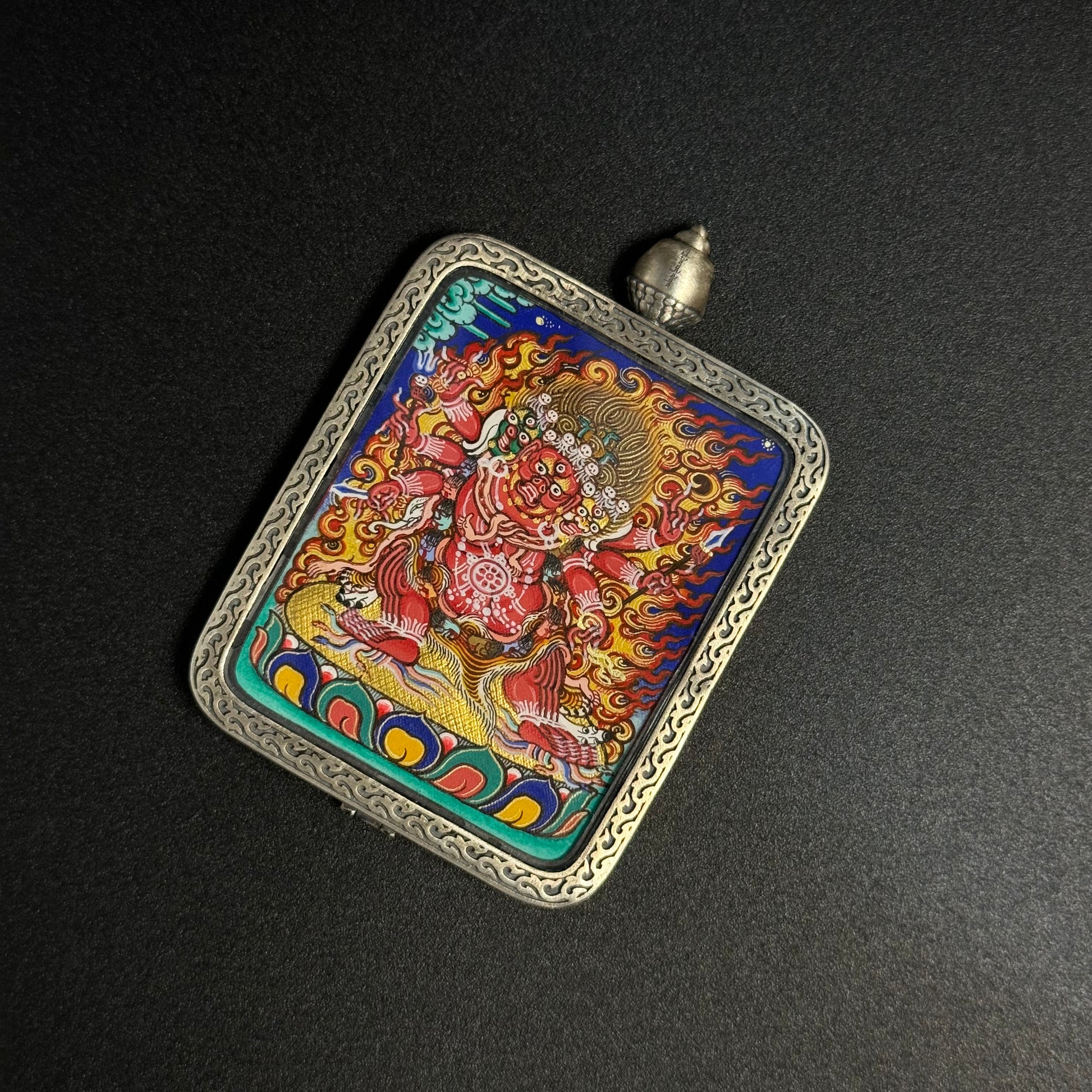 Angled close view of Hayagriva mini thangka pendant showing the wrathful horse-headed deity surrounded by flame halo, detailed mineral pigment painting and ornate sterling silver pendant frame.