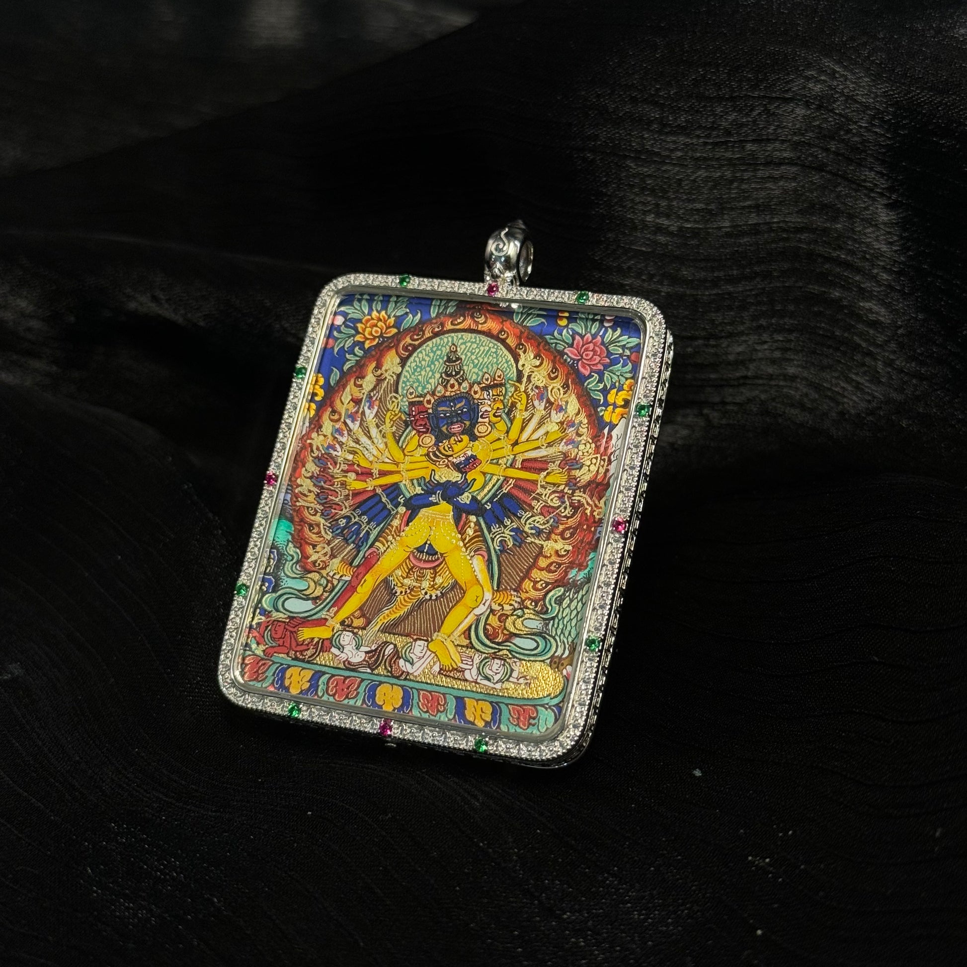 Kalachakra mini thangka pendant displayed on dark fabric background highlighting colorful mineral pigment painting and silver frame