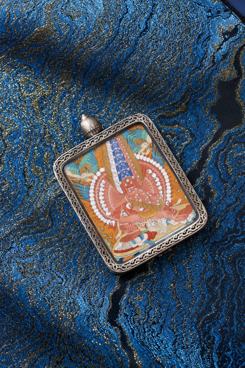 Angled close-up of Maha Heruka mini thangka pendant showing refined Tibetan linework, layered mineral pigments, and detailed wrathful yidam iconography