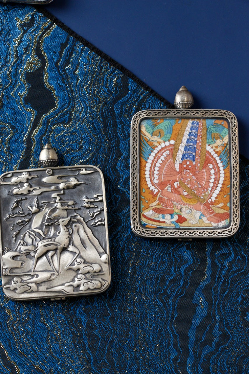Maha Heruka thangka pendant shown beside the Dunhuang Nine-Colored Deer silver gawu case, highlighting Tibetan mineral pigment artwork and protective case design