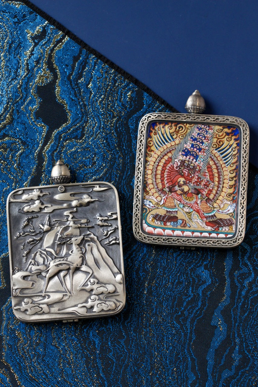 Maha Heruka mini thangka pendant alongside its Dunhuang Nine-Colored Deer silver gawu case, showing hand-crafted metalwork and thangka format