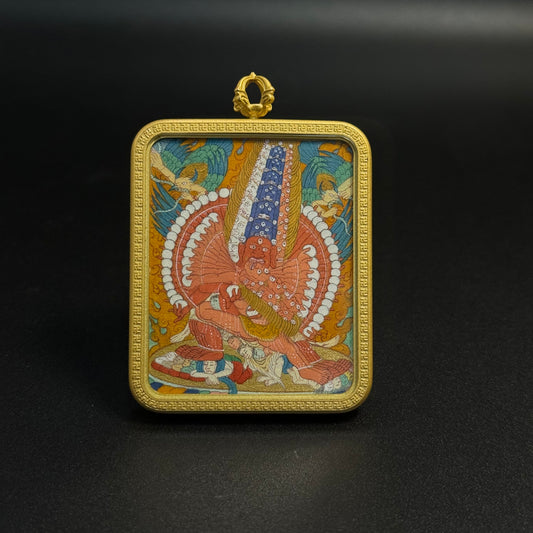 Front view of Mahakala mini thangka pendant showing the wrathful protector deity in traditional Tibetan iconography, hand-painted with mineral pigments and framed in a gold-toned protective pendant case.