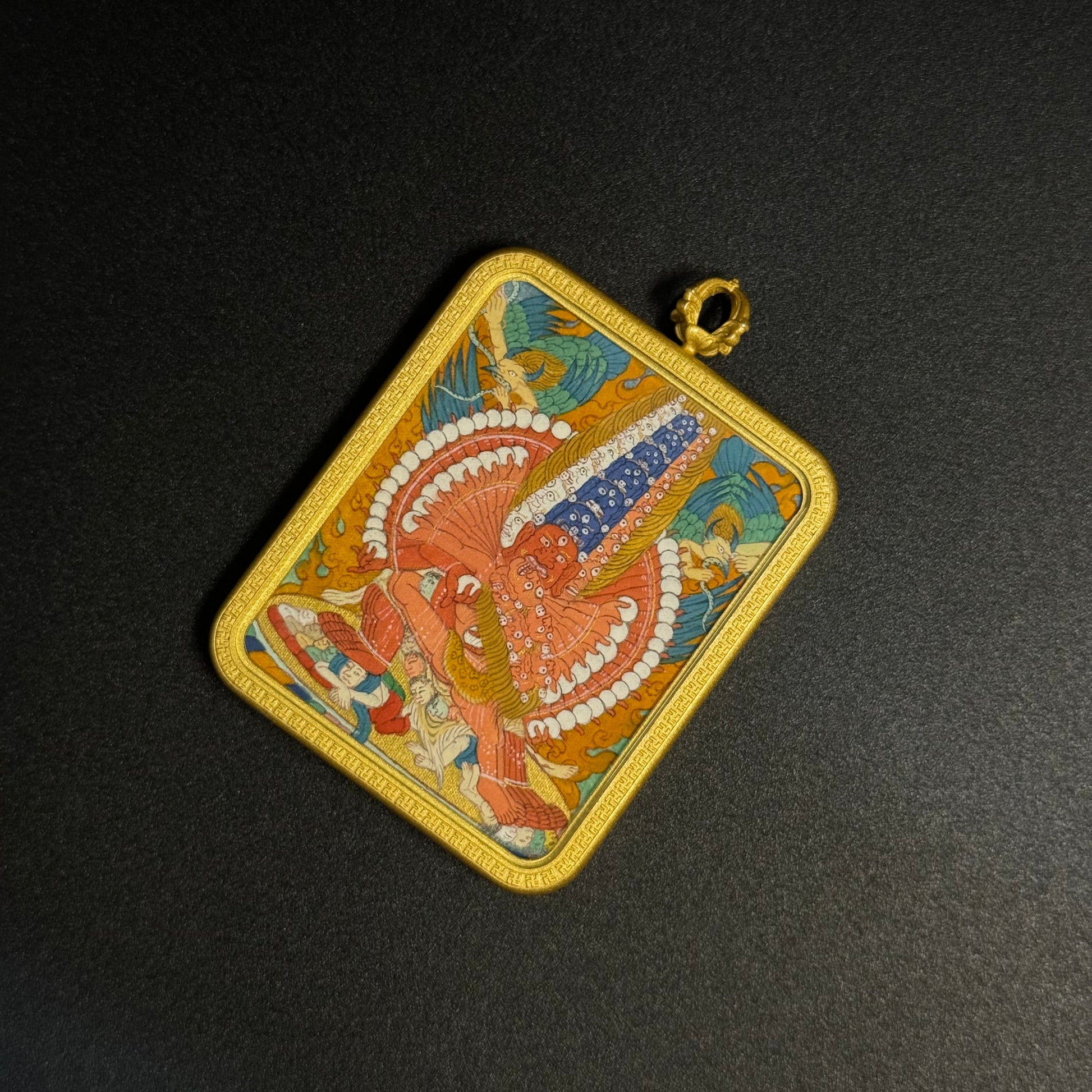 Close angled view of Mahakala mini thangka pendant highlighting intricate hand-painted details, vivid mineral pigment colors and the protective gold-toned pendant housing.