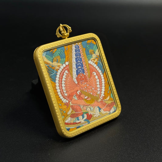 Angled view of Mahakala thangka pendant revealing detailed mineral pigment painting of the wrathful protector deity surrounded by flame aura and enclosed in a gold-colored pendant frame.