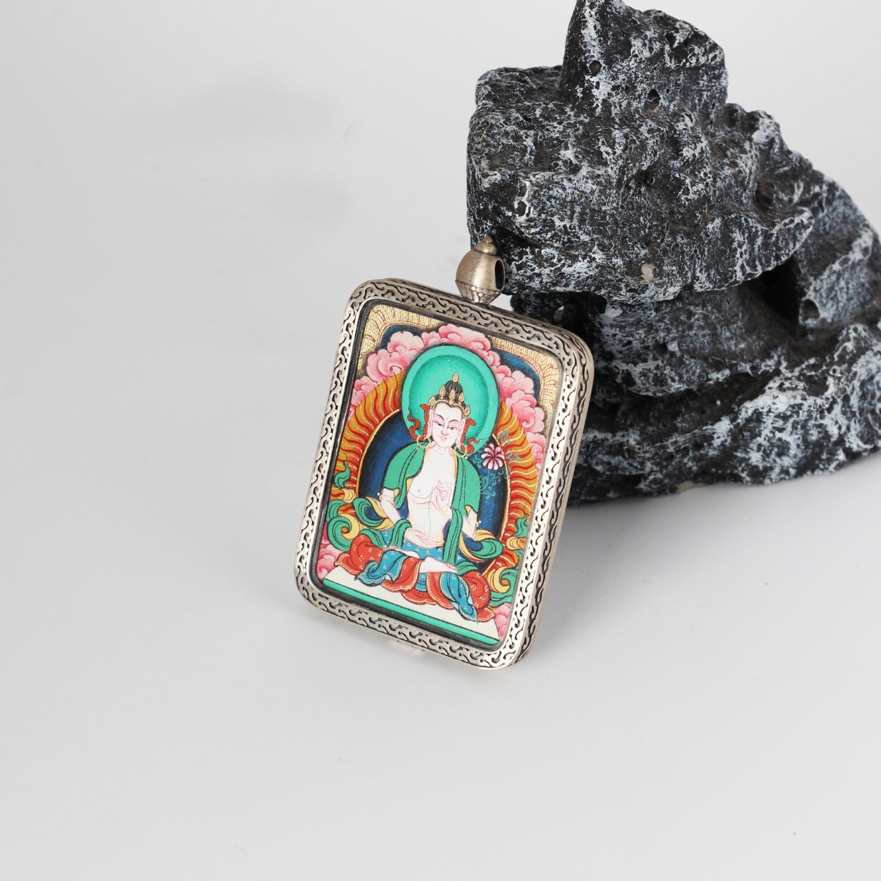 Mahasthamaprapta mini Thangka pendant displayed on a stone prop, emphasizing the vivid hand-painted artwork, green-blue halo tones, and the detailed engraved pure silver frame.