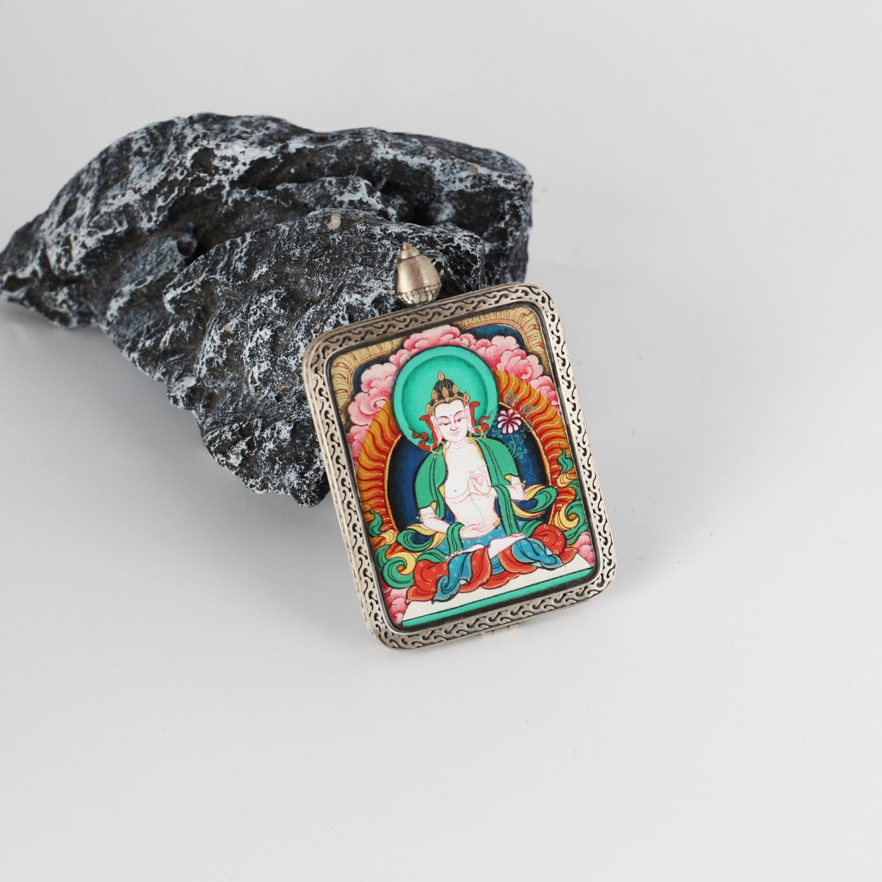 Angled view of Mahasthamaprapta mini Thangka pendant highlighting layered mineral pigment colors, fine facial and robe details, and the ornate engraved silver border around the rectangular pendant.