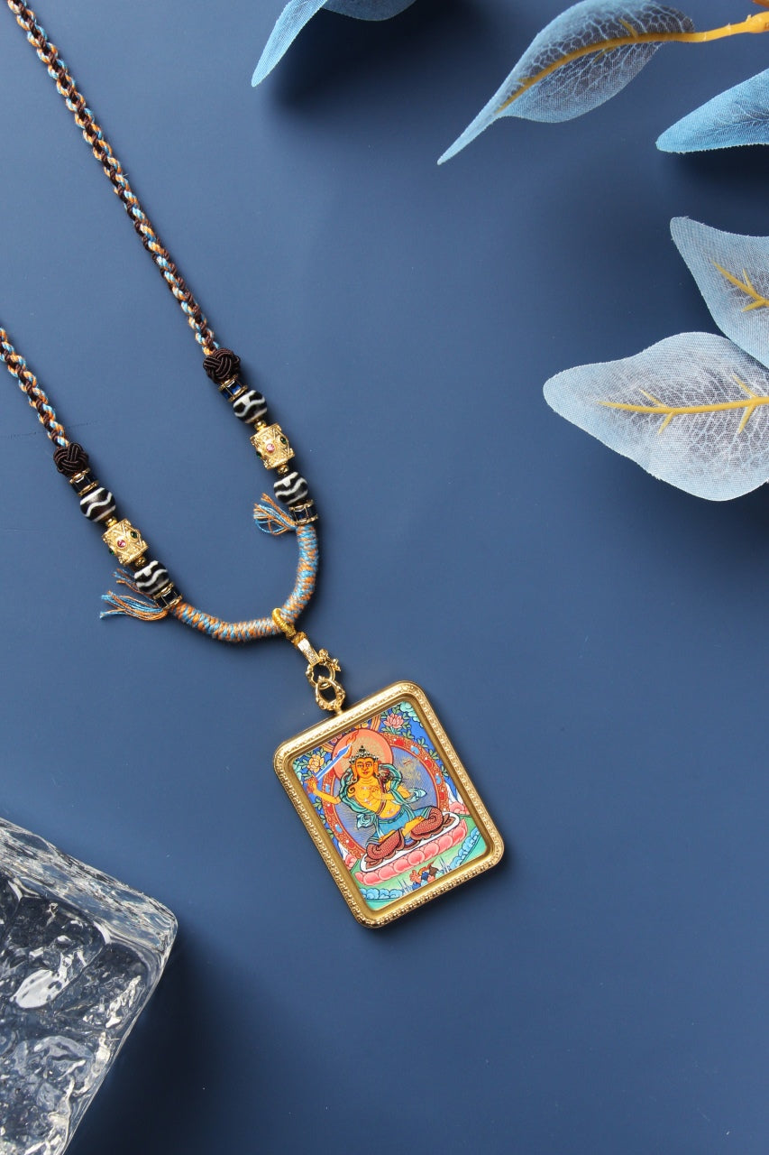 Angled front view of the Manjushri Bodhisattva mini thangka pendant highlighting the hand-painted image, vivid mineral pigment colors, metal case thickness, textured border pattern, and clasp-to-bail hardware connection.