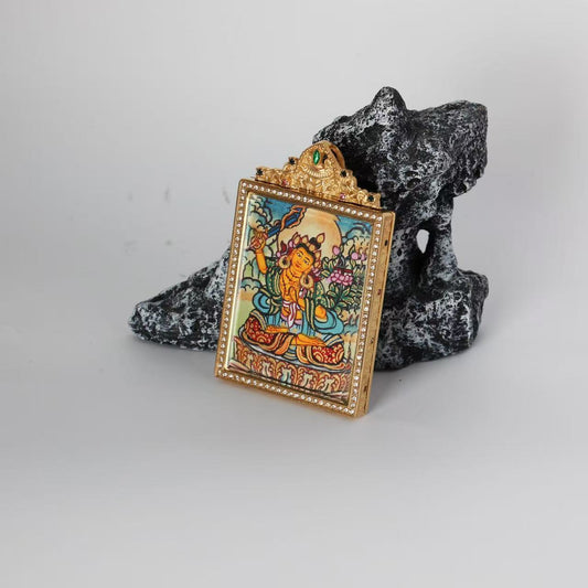 Angled view of the Manjushri mini Thangka pendant highlighting the raised jeweled top ornament, crystal-lined frame, and the thickness of the double-sided titanium steel case.