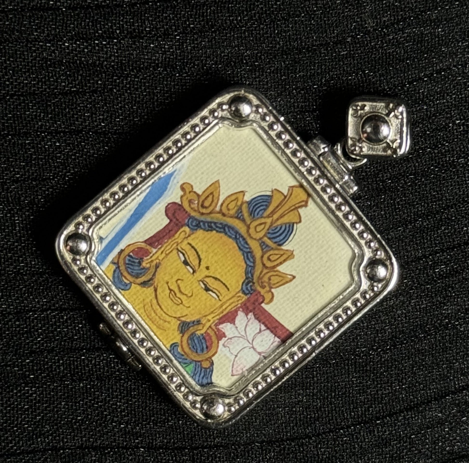 Close-up detail of the Manjushri Bodhisattva portrait in a miniature thangka pendant, showing mineral pigment painting and silver framed setting.
