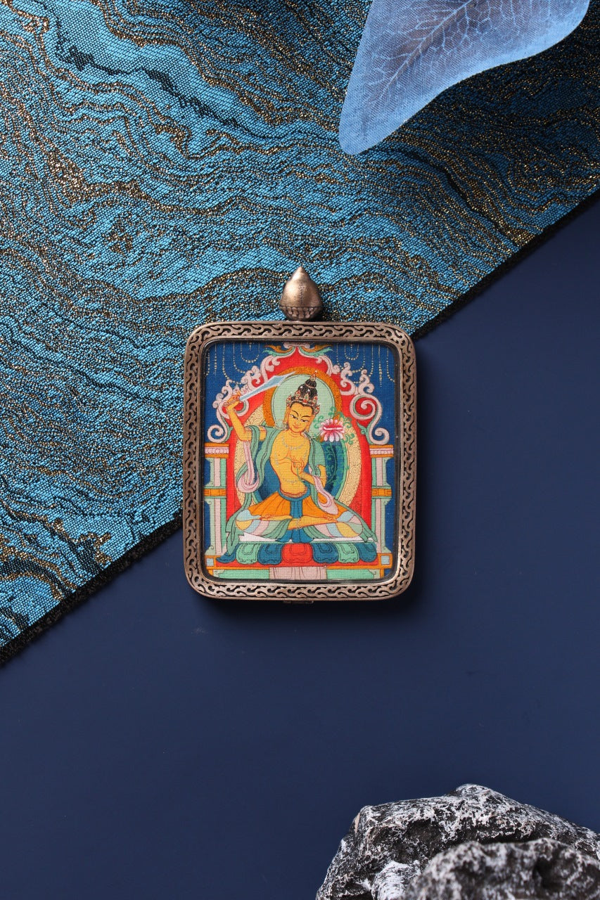 Front view of Manjushri Bodhisattva mini thangka pendant with detailed silver frame and blue thangka background