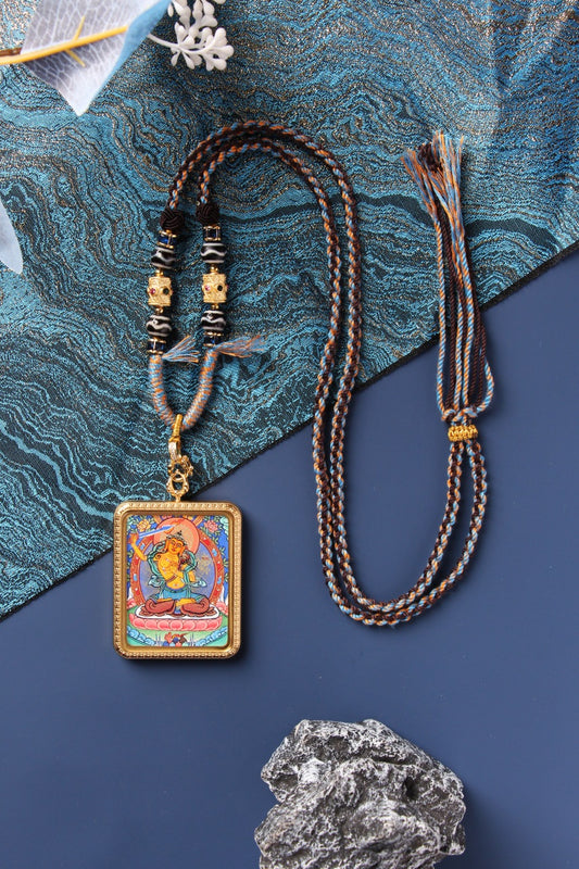 Manjushri Bodhisattva mini thangka pendant shown in full view, featuring the hand-painted deity image with mineral pigment colors, rectangular titanium steel case, raised border detailing, braided cord, bead section, and adjustable cord ends.