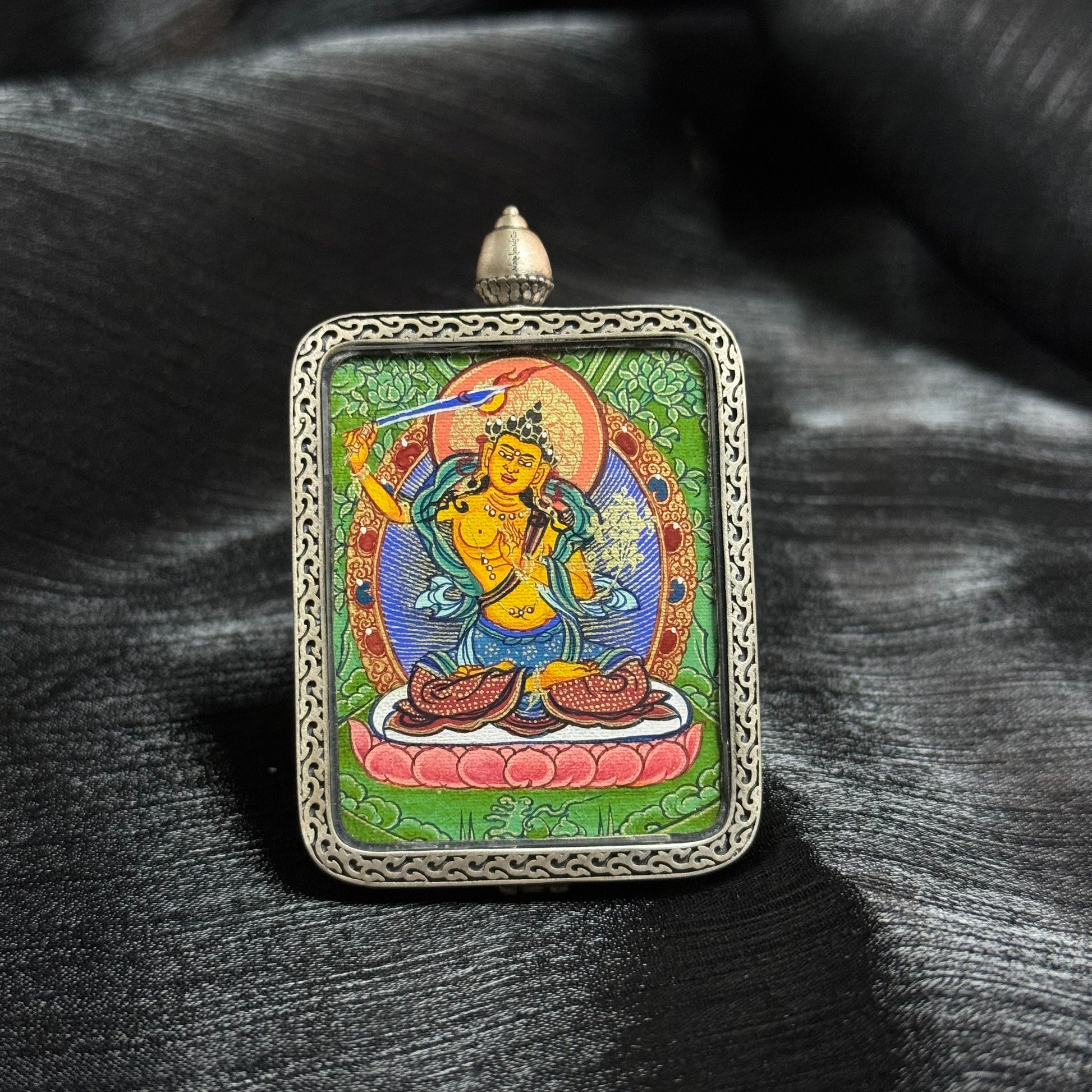 Front view of Manjushri Bodhisattva mini thangka pendant showing hand-painted Rebgong thangka artwork with mineral pigments and silver frame details
