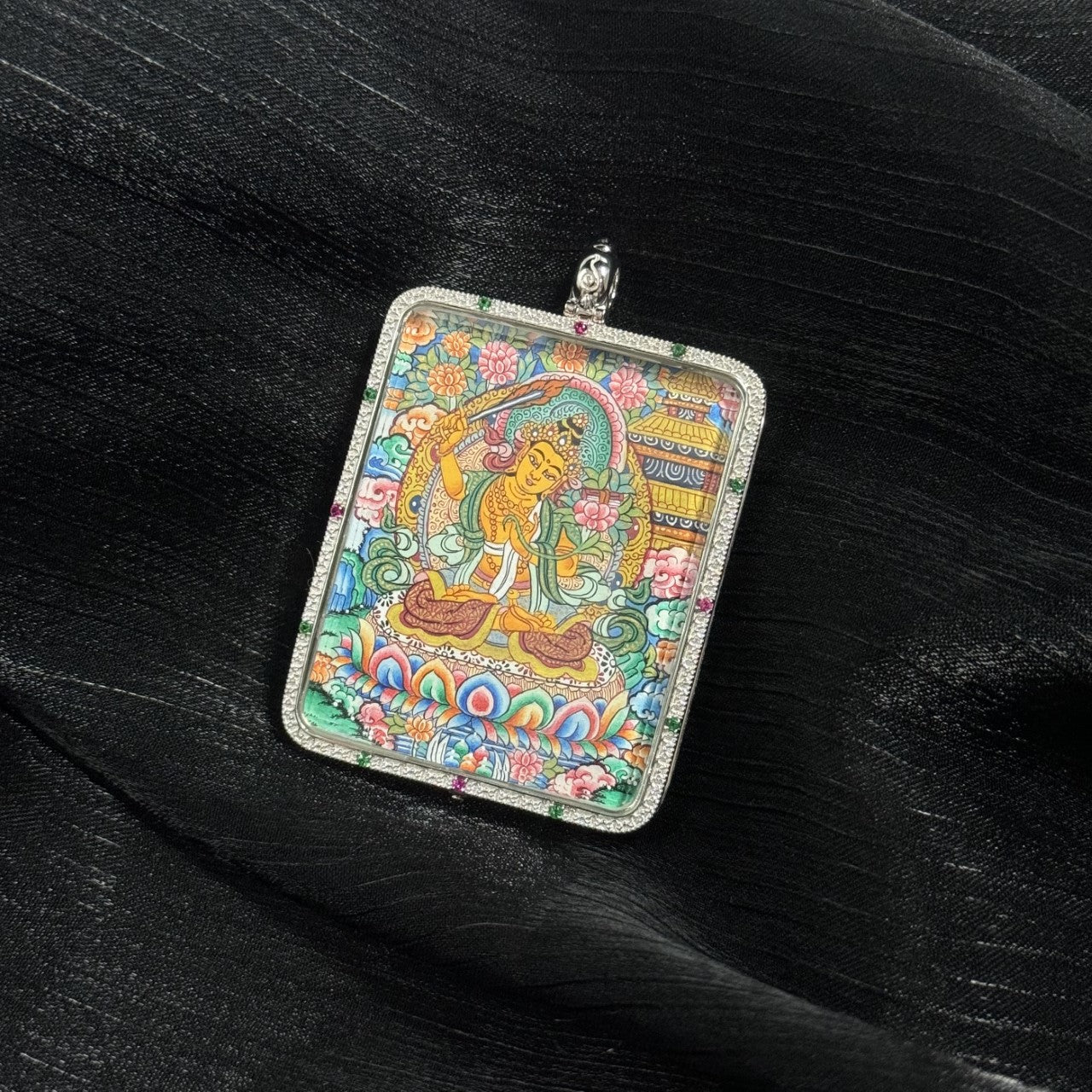 Hand-painted Manjushri Bodhisattva miniature thangka pendant featuring the wisdom deity seated on a lotus throne with vibrant mineral pigments and a decorative silver frame.