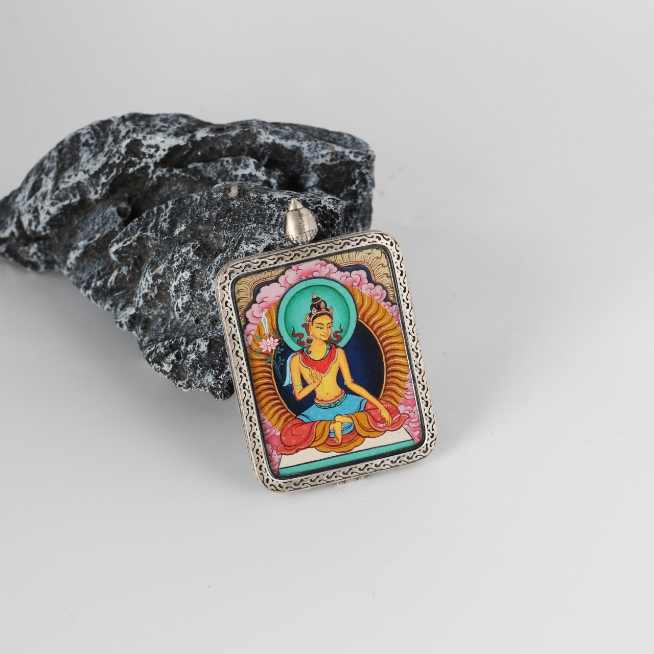 Tilted view of a Manjushri Bodhisattva mini Thangka pendant, showing the engraved silver gawu-style frame, pendant loop structure, and the framed hand-painted Thangka artwork.
