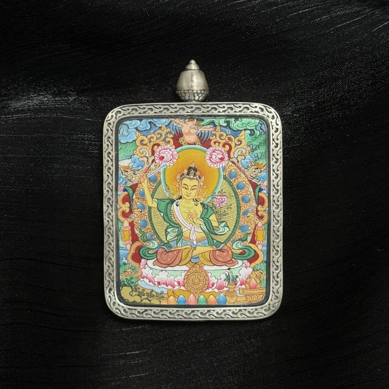 Front view of Manjushri Bodhisattva mini thangka pendant, hand-painted with mineral pigments, holding wisdom sword and lotus, enclosed in Dunhuang Nine-Colored Deer silver gawu case with engraved border.