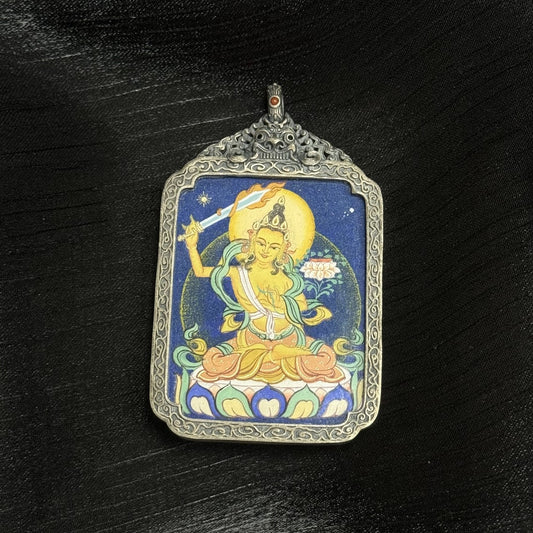 Close-up of Manjushri Bodhisattva mini thangka pendant, hand-painted with mineral pigments, set in an ornate vintage silver case with detailed carved border and blue background.