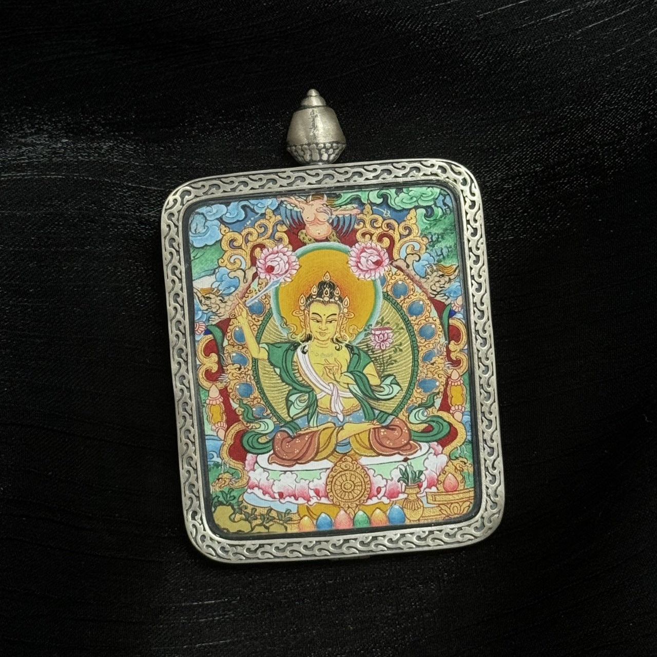Side perspective of Manjushri Bodhisattva Tibetan Miansa mini thangka pendant emphasizing color saturation, sword silhouette, lotus platform, and engraved silver border craftsmanship.
