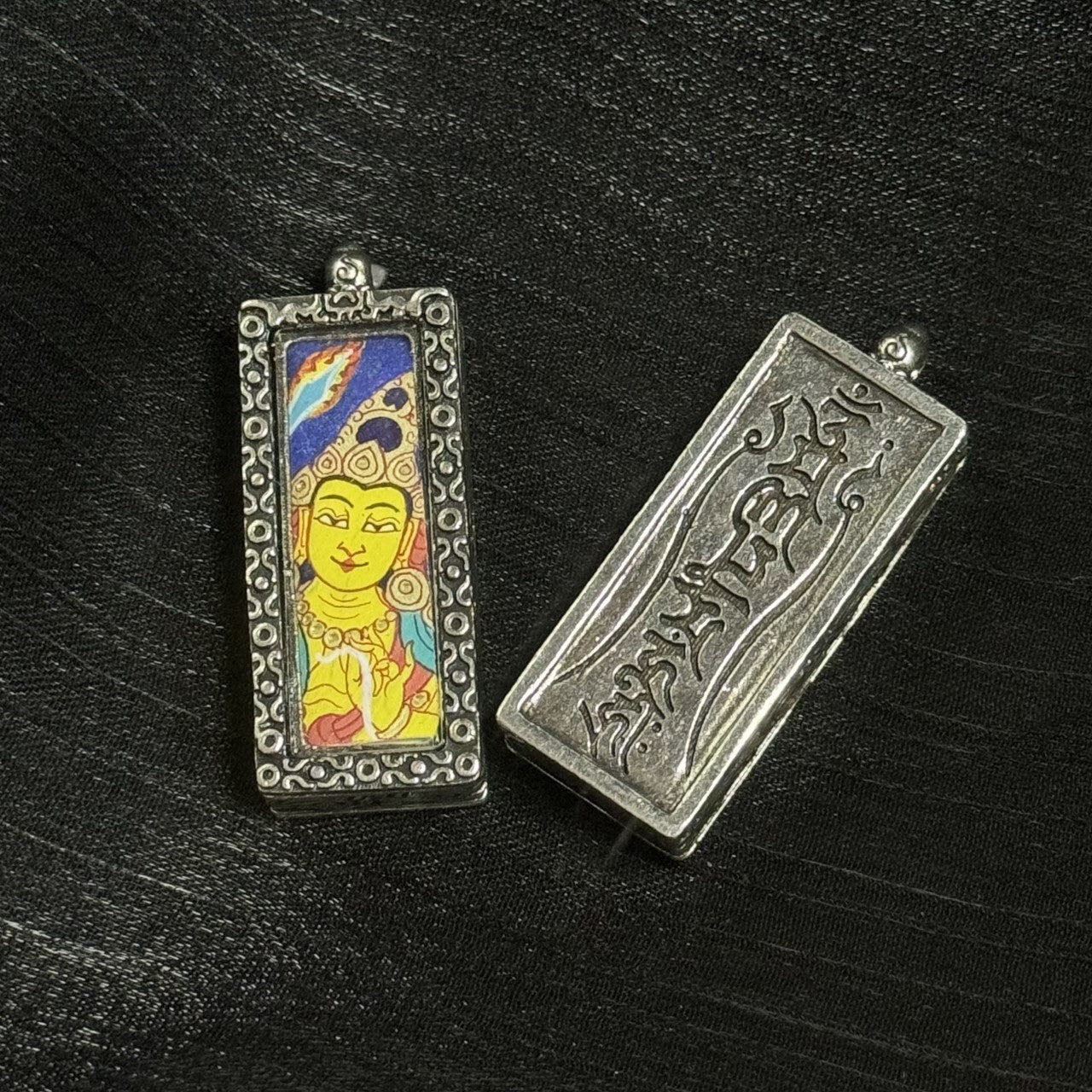 Front and back view of a Manjushri mini thangka pendant, showing the hand-painted Manjushri portrait on how the pendant face is framed by an ornate metal border, and the back panel with engraved script design.