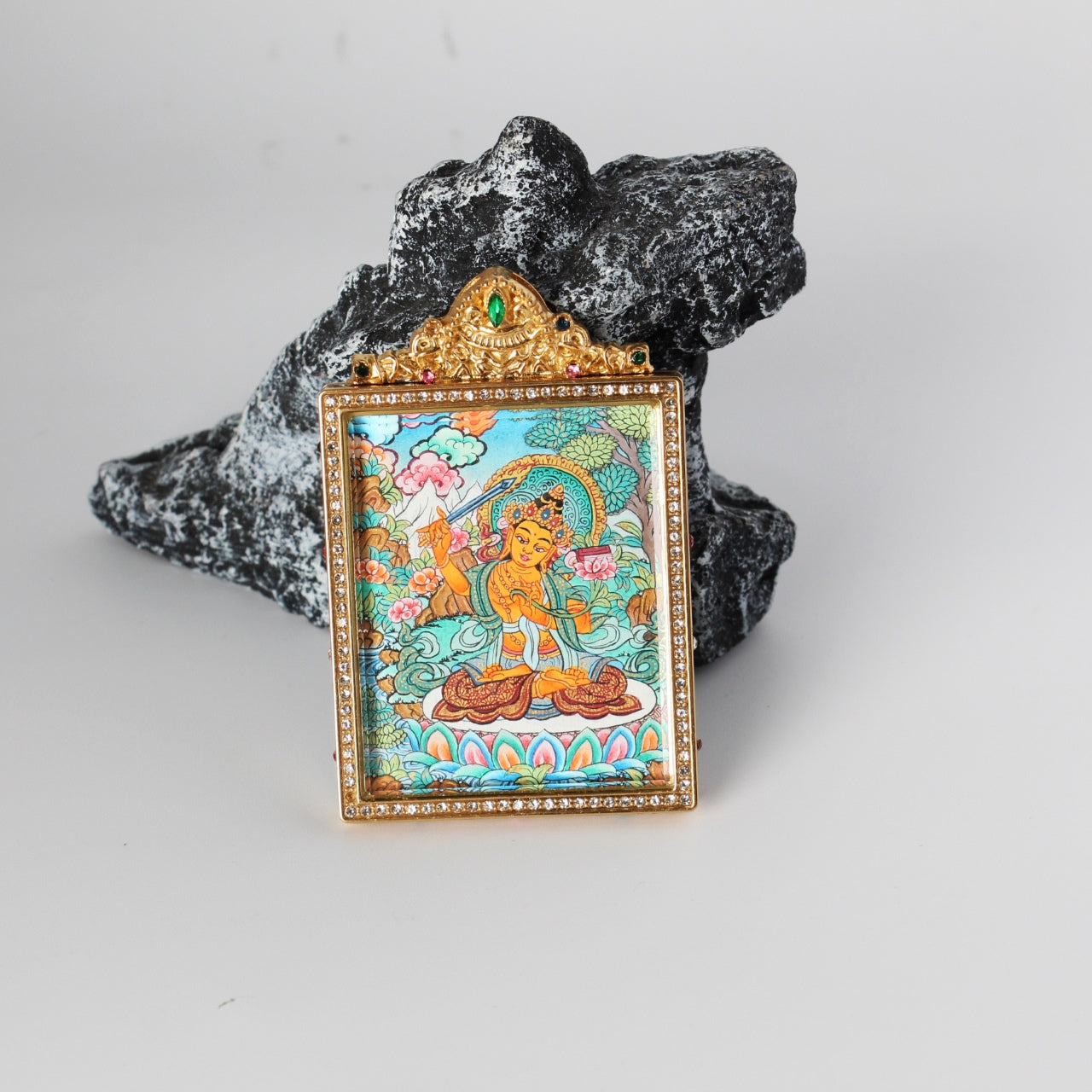 Front view of a Nepal hand-painted Manjushri (Manjushri Bodhisattva) thangka pendant in a jeweled gold frame, displayed against a black stone background.