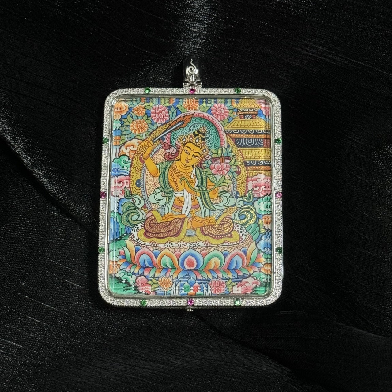 Manjushri Bodhisattva thangka pendant artwork showing the wisdom deity holding the flaming sword of insight, painted with mineral pigments in a silver jewelry frame.