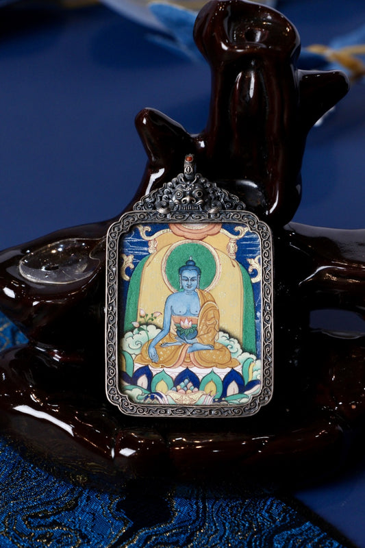 Close-up of Medicine Buddha (Bhaisajyaguru) hand-painted thangka pendant in a vintage silver gawu case, Tibetan mineral pigments