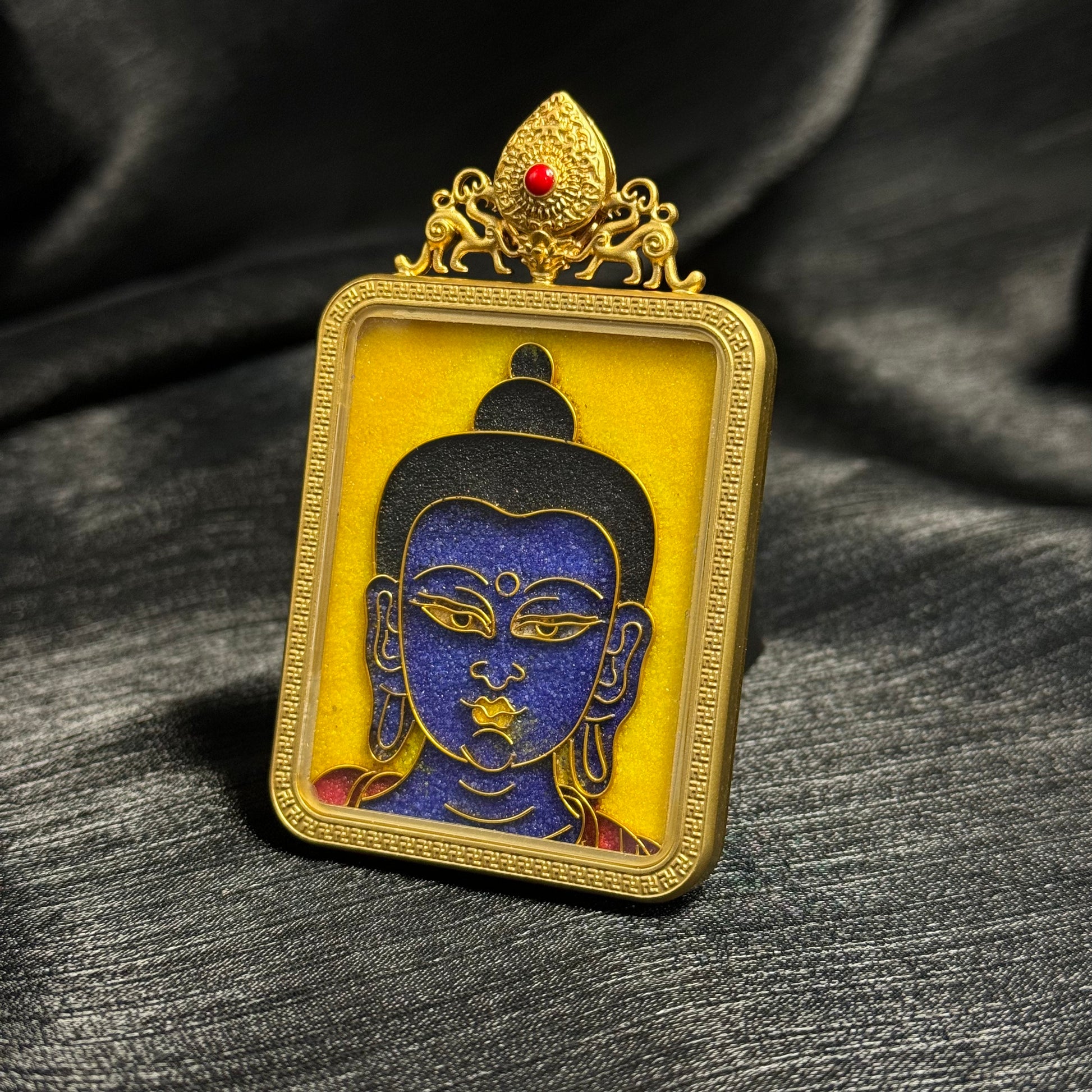 
Angled close-up of Medicine Buddha cloisonné enamel pendant showing gold wire cloisonné lines, blue enamel Buddha face, and gold-plated copper protective frame