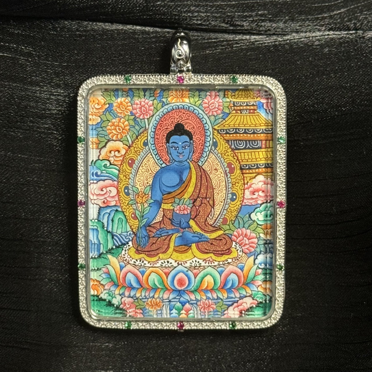 Detailed close-up of a Medicine Buddha mini thangka pendant highlighting the blue Buddha figure, lotus base, intricate halo, and finely painted mineral pigment details.