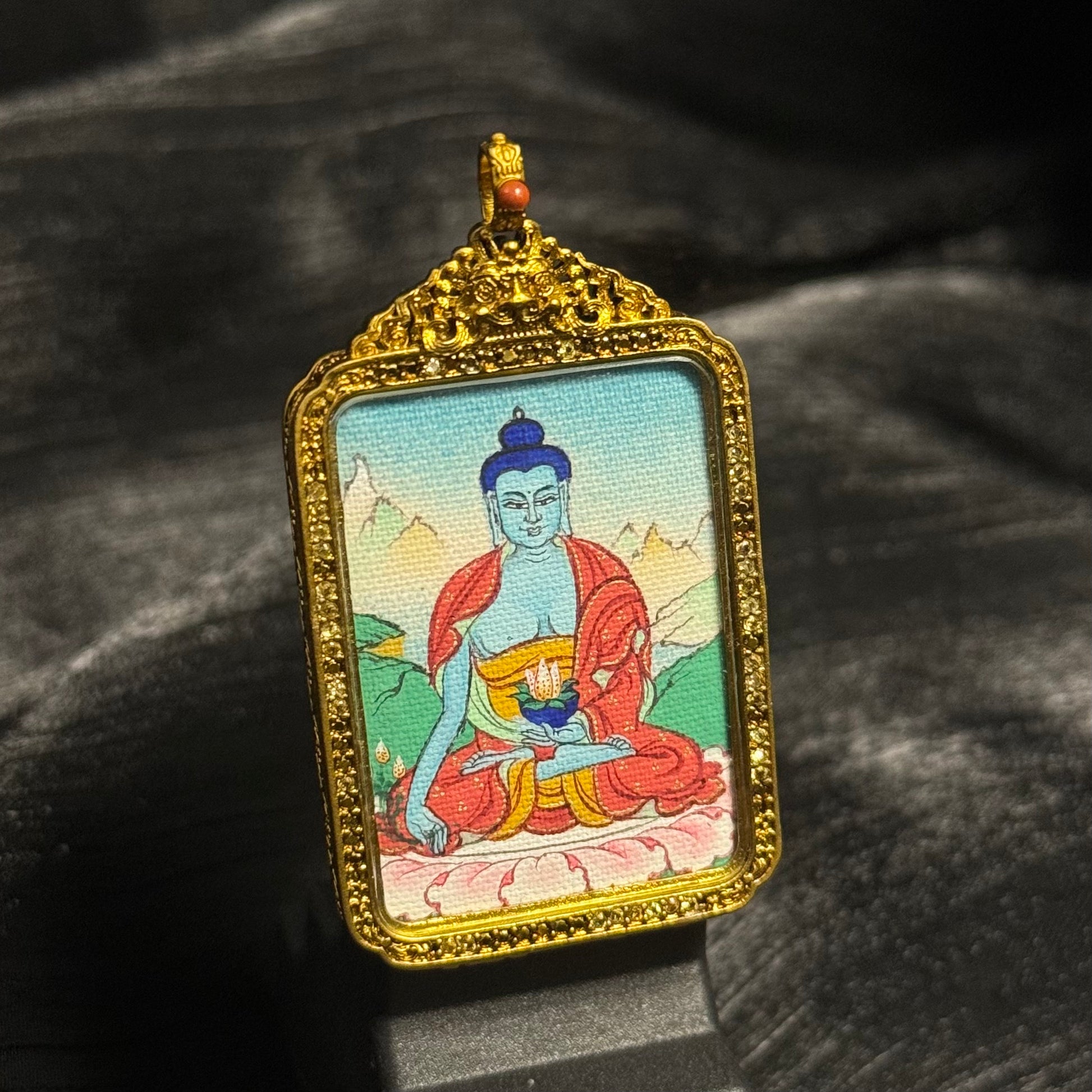 Angled view of Medicine Buddha miniature thangka pendant showing detailed mineral pigment painting and ornate Tibetan copper frame