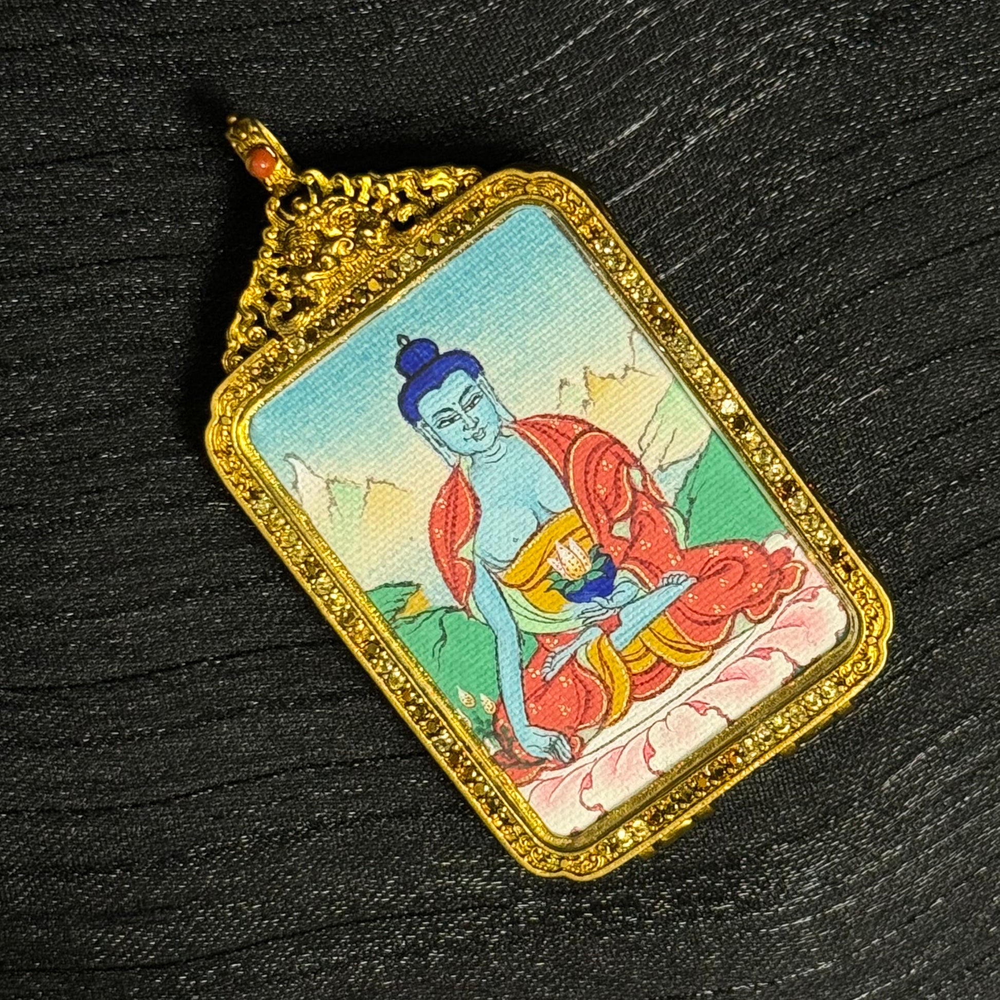 Detailed angled view of Medicine Buddha miniature thangka pendant mounted in an ornate Tibetan copper protective case
