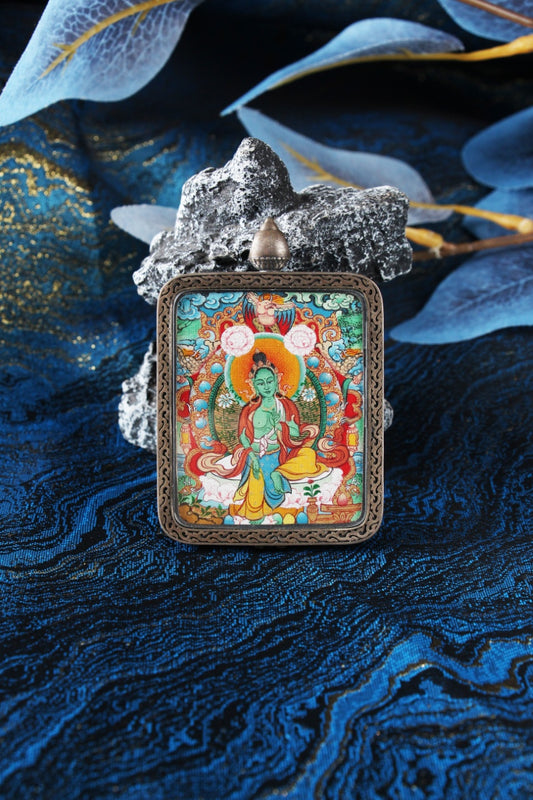 Front view of a Menri style Green Tara mini thangka pendant, hand-painted with natural mineral pigments in Tibet, set in a Dunhuang Nine-Color Deer silver case on blue textile and stone background.