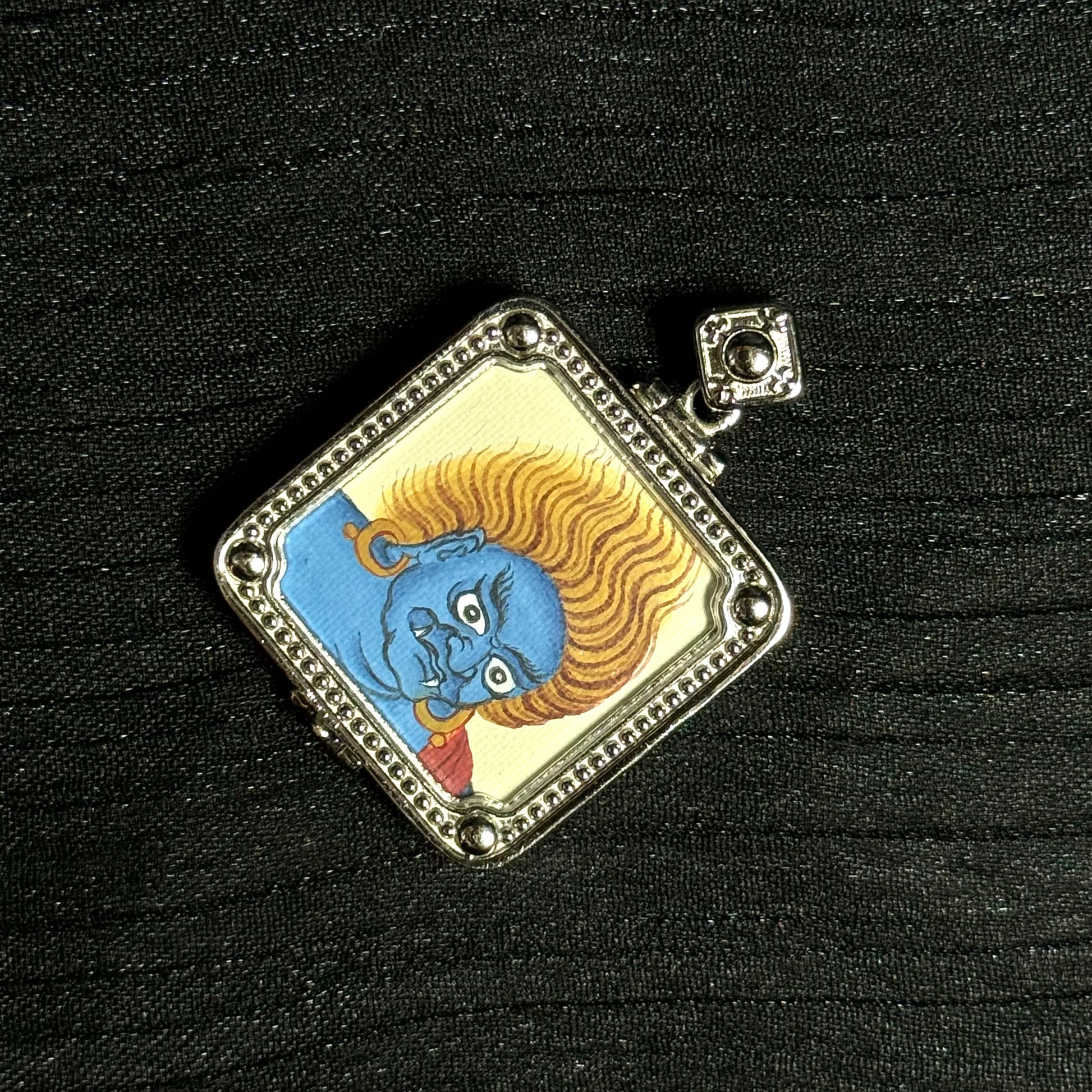 Mini Acalanatha thangka pendant displayed on black fabric background Tibetan Buddhist art