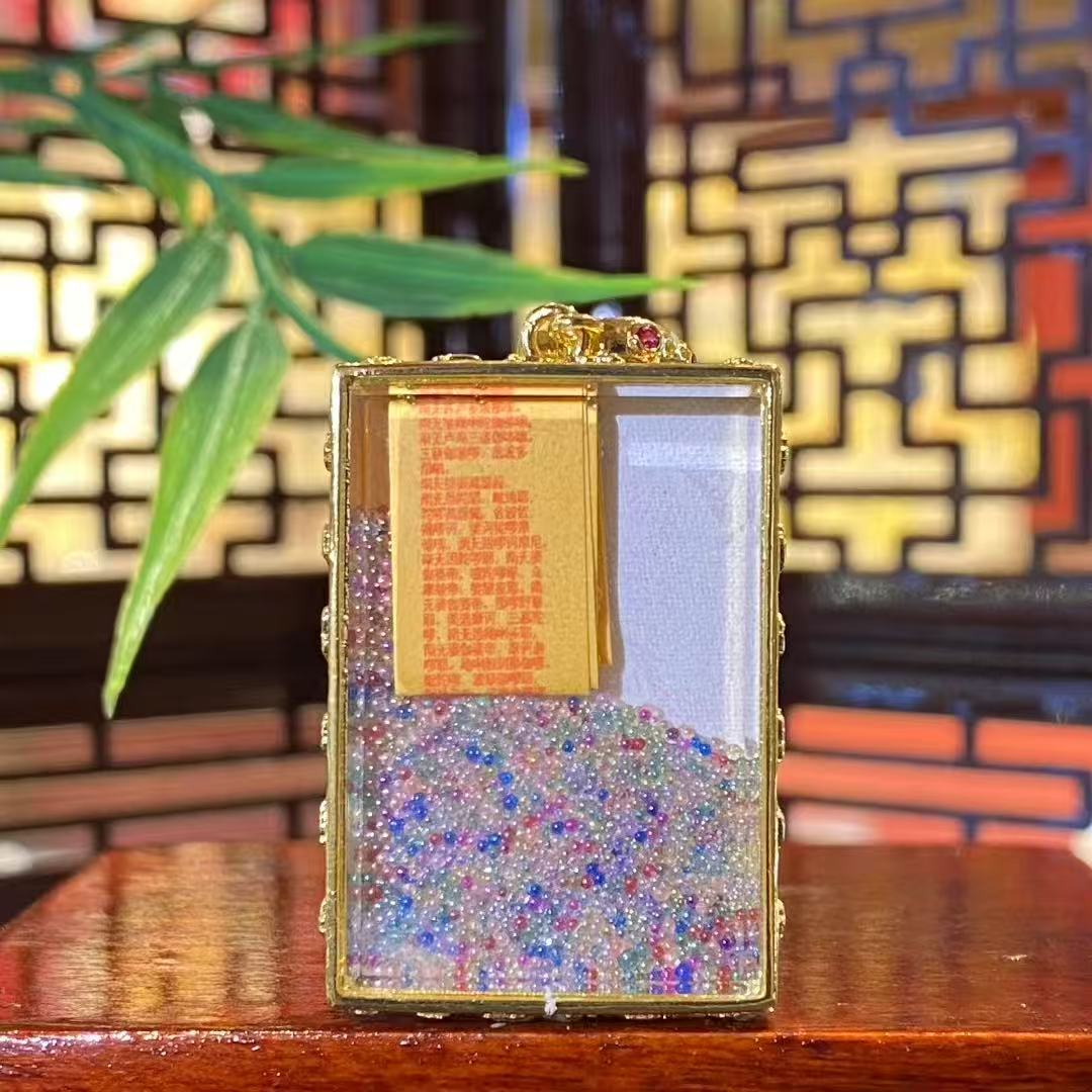 Back view of an open mini Green Tara Gau Thangka pendant showing seven treasures glass beads and a khata inside the copper gau box