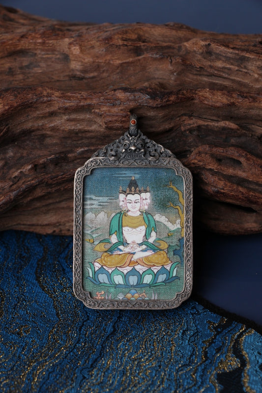 Close-up of a multi-faced deity mini thangka pendant set in a vintage silver gawu box, highlighting the mineral pigment painting and ornate top loop.