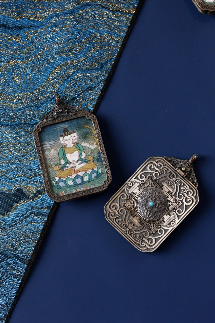 Front and back view of a multi-faced deity mini thangka pendant in a vintage silver gawu box, hand-painted with mineral pigments on a blue textile background.