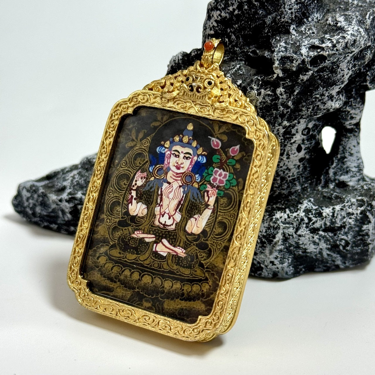 Angled close-up of Nepal Black Gold Series Four-Armed Avalokiteshvara pendant showing dark gold-toned background patterns, lotus seat, and intricate gold frame relief.