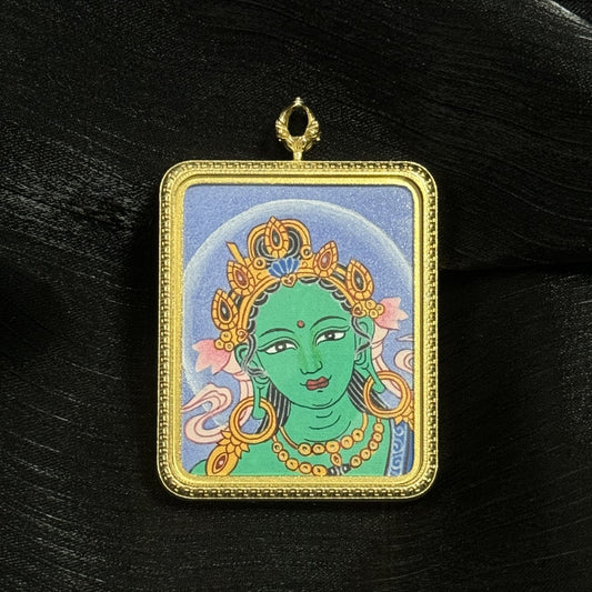 Detailed miniature Green Tara head thangka painting inside a gold-tone titanium steel pendant case, showing delicate Himalayan thangka brushwork and decorative border.
