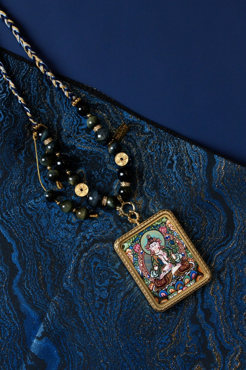 Flat lay styling of Akashagarbha Bodhisattva mini thangka pendant necklace on blue textile background