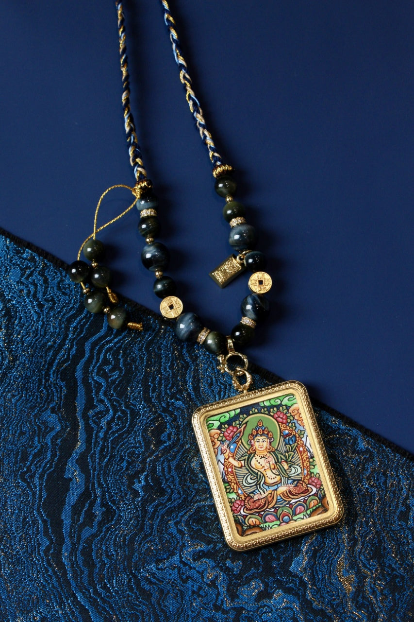Flat lay styling of Manjushri Bodhisattva mini thangka pendant necklace on blue textile background
