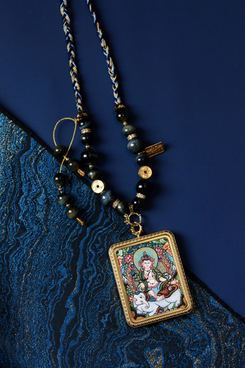 Flat lay styling of Samantabhadra Bodhisattva mini thangka pendant necklace on blue textile background